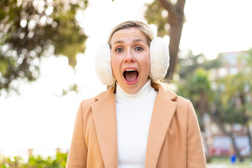 Wall Mural - Young blonde woman wearing winter muffs at outdoors with surprise facial expression