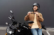 Stylish smiling confident man, biker wearing helmet standing near sport motorcycle. Handsome successful fashion model wearing stylish leather jacket, sunglasses posing for pictures on motorbike