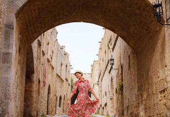 Wall Mural - summer trip to Rhodes island, Greece. Young Asian woman in ethnic red dress walks Street of Knights of Fortifications castle. female traveler visiting southern Europe. Unesco world heritage site.