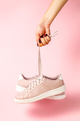 Wall Mural - Fenale Hand with stylized fingernails holding hanging pink sneakers by the laces on white background. Hand with a new sport shoe.