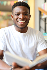 Handsome African American man wearing a white t-shirt and holding a book. He is a young and smart student, learner or fashion who is smiling, laughing or looking for his education.