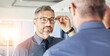 © JessicaLeigh J/peopleimages.com - Mirror reflection, optometry and man with glasses for eye care, vision and choice of frame. Mature, store and person eyewear shopping for a lens or fit for eyeglasses style in a shop with a decision