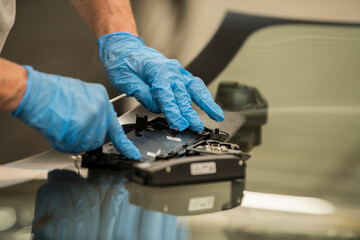 Hand from a mechanic with blue nitril gloves handling the camera and other equipment mounted on a front windshield of a car. auto repair shop. automotive industry.