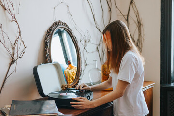 A modern teenage girl with dyed hair turns on a retro record player, meeting modern with retro