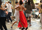 Fototapeta Natura - Couples dancing on the street - tanned woman wearing red bright dress in the centre