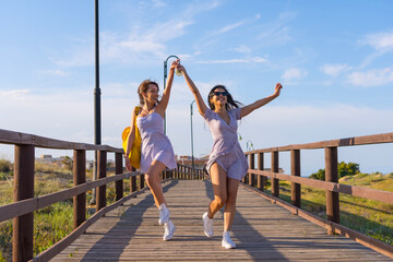 Wall Mural - Female friends on summer vacation at the beach walking on a wooden path walking and jumping with excitement