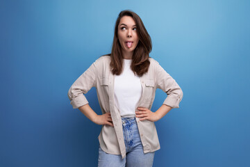 Wall Mural - brunette young female adult in a shirt and jeans with a grimace on the background with copy space