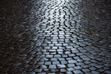 Fototapeta  - Cobblestone in a narrow street in Stresa, Italy. Wet shiny historic basalt ashlars or blocks reflecting blue sky and sunshine after rain. Old pavement background with typical surface and structure.