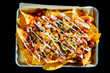 © Andrew Kornylak - Pulled pork nachos on a tray with parchment paper against a black background, with sour cream drizzled on top