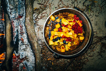 Fruit Cobbler Cooking In A Pan Over Hot Coals In A Campfire On A Sandy Beach At Night, Closeup