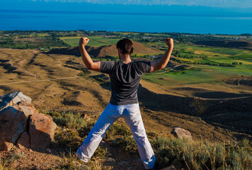 Canvas Print - Young man traveler showing his strength on top of the mountain