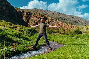 Canvas Print - Man hiker standing and balancing on both sides of a mountain stream