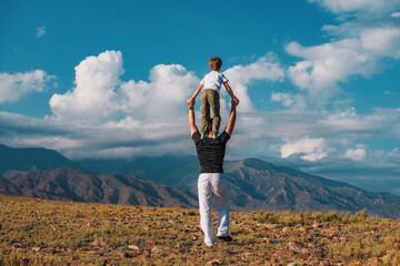 Boy standing on his father's shoulders on mountains background