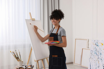 Poster - Young woman painting on easel with canvas in studio