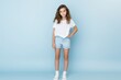 © Tuyres - Portrait of a fictional elegant cute young girl wearing a white blank t-shirt and jeans short. Isolated on a light blue background. Generative AI.