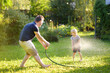 © Maria Sbytova - Funny little boy with his father playing with garden hose in sunny backyard. Preschooler child having fun with spray of water.