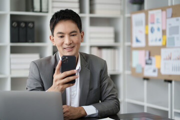 Wall Mural - Smart young Asian businessman using smartphone while working in the office room.