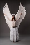 Fototapeta Pokój dzieciecy - White angel with wings rising her heands and looking up the sky