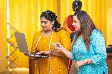 Two Indian female fashion designer using laptop at her shop.