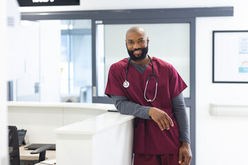 Wall Mural - Portrait of happy african american male doctor wearing scrubs in reception at hospital