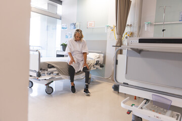 Wall Mural - Senior caucasian female patient with prosthetic leg sitting on bed at hospital