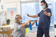 © WavebreakMediaMicro - Caucasian physiotherapist and senior woman with face masks using exercise band stretching arms