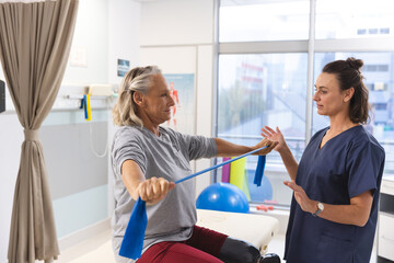 Wall Mural - Caucasian female physiotherapist and senior woman with artificial leg using exercise band stretching