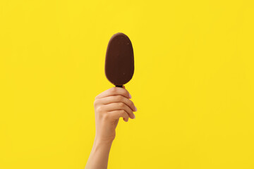 Woman holding delicious chocolate covered ice cream on stick against yellow background