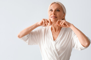 Canvas Print - Mature woman doing face building exercise on light background