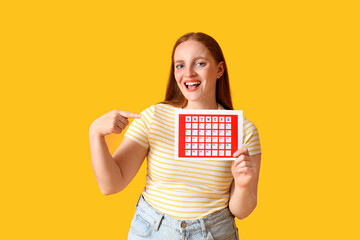 Wall Mural - Young woman pointing menstrual calendar on yellow background