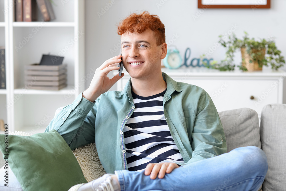 Young redhead man talking by mobile phone on sofa at home