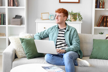 Sticker - Young redhead man using laptop on sofa at home