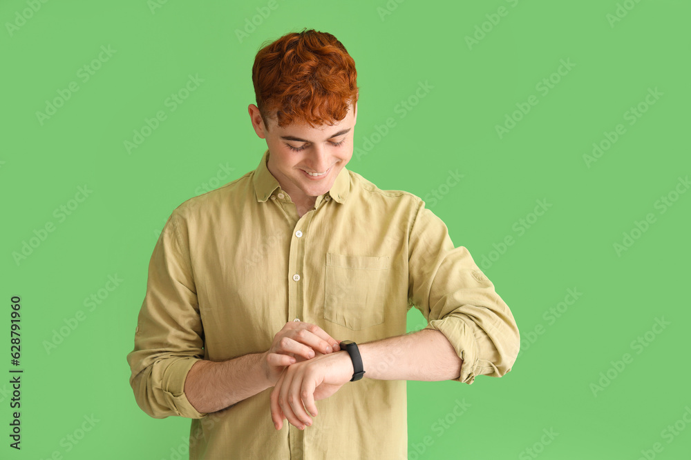 Young redhead man looking at smartwatch on green background