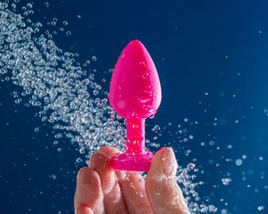 Woman washing pink anal plug under shower on blue background. 