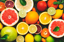Colorful Citrus Fruis, Food Background, Top View. Mix Of Different Whole And Sliced Fruits: Orange, Grapefruit, Lemon, Lime And Other With Leaves On  Green Stone Table