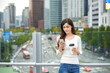 © Dialogue Frame - A young woman is resting on a land bridge with coffee and a smartphone in the background of a busy street during the day.