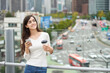 © Dialogue Frame - A young woman is resting on a land bridge with coffee and a smartphone in the background of a busy street during the day.