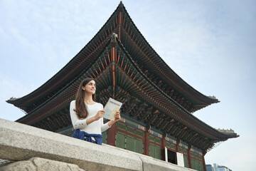 A young woman who travels in a traditional Korean village and looks for directions while looking at a map	