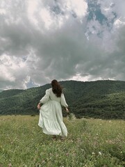 Sticker - Young woman in a white dress walks in a green field with wildflowers.