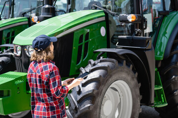 Poster - Woman farmer with a digital tablet on the background of an agricultural tractors.