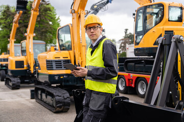 Aufkleber - Engineer in a helmet with a digital tablet stands next to construction excavators.