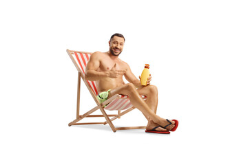 Wall Mural - Young man holding a bottle of sun cream seated at a beach chair