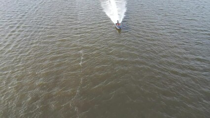 Canvas Print - Drone footage of speed boats sailing in the water with green hills on the horizon with cloudy sky