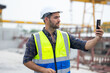 © NVB Stocker - building and construction worker using mobile phone, Hiapanic latin male wearing safety hard hat helmet standing with arms crossed at construction site and looking at camera