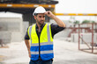 © NVB Stocker - Portrait building and construction worker, Hiapanic latin male wearing safety hard hat helmet standing with arms crossed at construction site and looking at camera