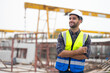 © NVB Stocker - Portrait building and construction worker, Hiapanic latin male wearing safety hard hat helmet standing with arms crossed at construction site and looking at camera
