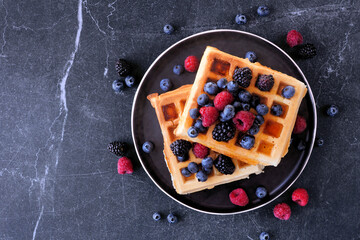 Poster - Breakfast waffles with raspberries and blueberries. Top view over a dark stone background.