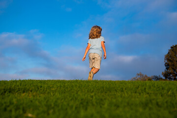 Happy child boy runs around the green field, emotional walk on nature and happiness. Cute little boy having fun outdoors on blue sky.