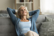 © fizkes - Peaceful satisfied elderly woman relaxing on couch with closed eyes, smiling, stretching body, leaning on soft back with open elbows, enjoying leisure, calm lazy break at home, breathing fresh air