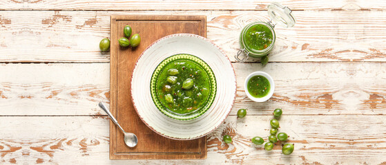 Tasty gooseberry jam on light wooden background